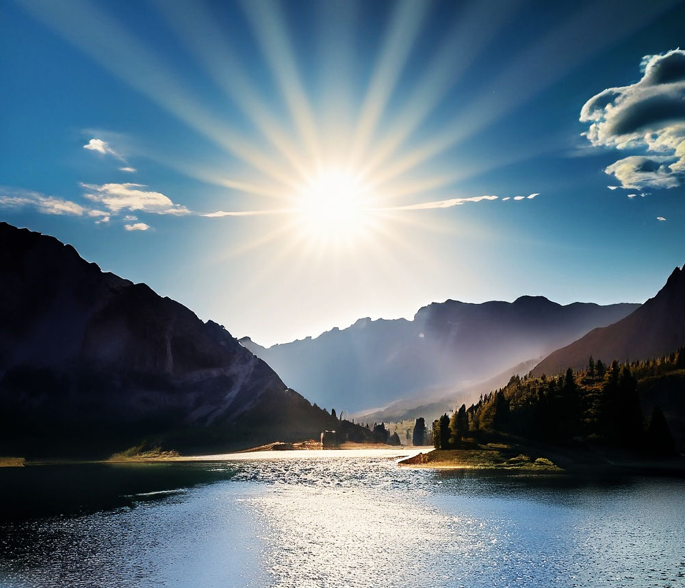 A landscape of a lake and mountains with a sunburst effect